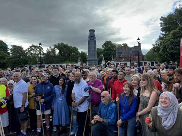 A large diverse crowd of townspeople in Middlesbrough gather with sweeping brushes and a smile.