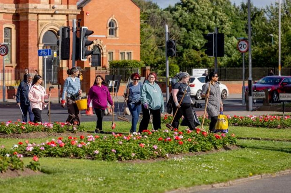 Photo of several volunteers walking across a public space in Middlesbrough holding sweeping brushes and bags.