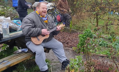 Man siting on bench playing a small guitar 