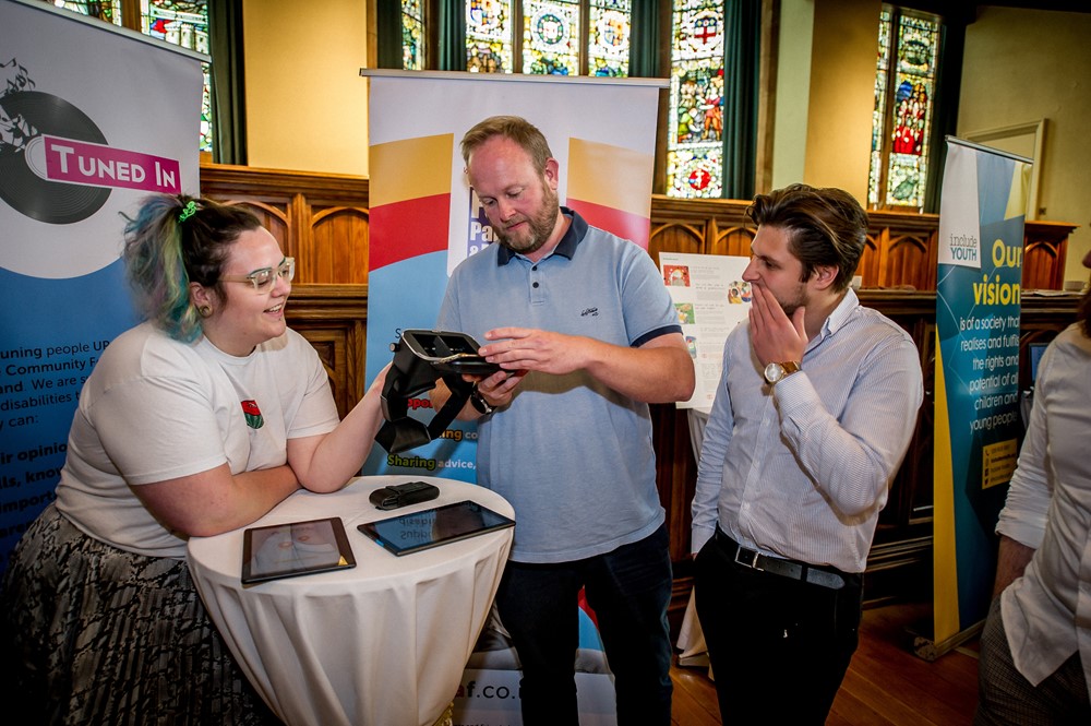 Woman passing VR headset to a man and another man watching