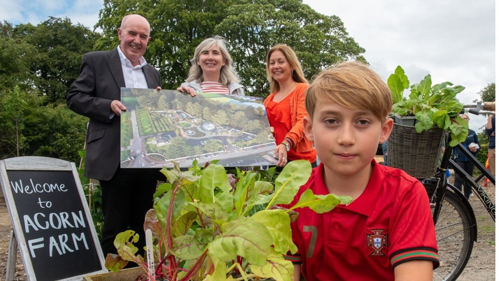 Photo of three adults and a child outside a community farm, smiling at the camera and holding bunches of lettuce.