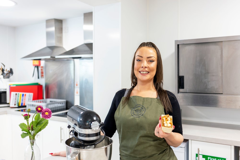 Woman holding a cake smiling at camera next to a food mixer