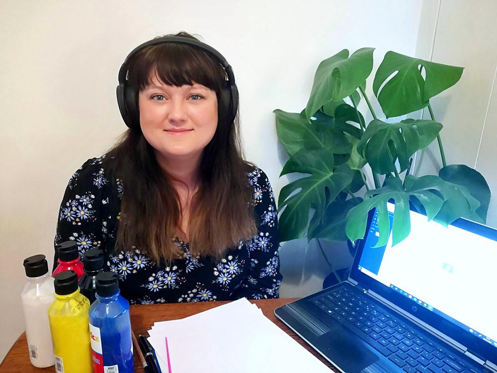 Woman with headset on in front of paints and a laptop